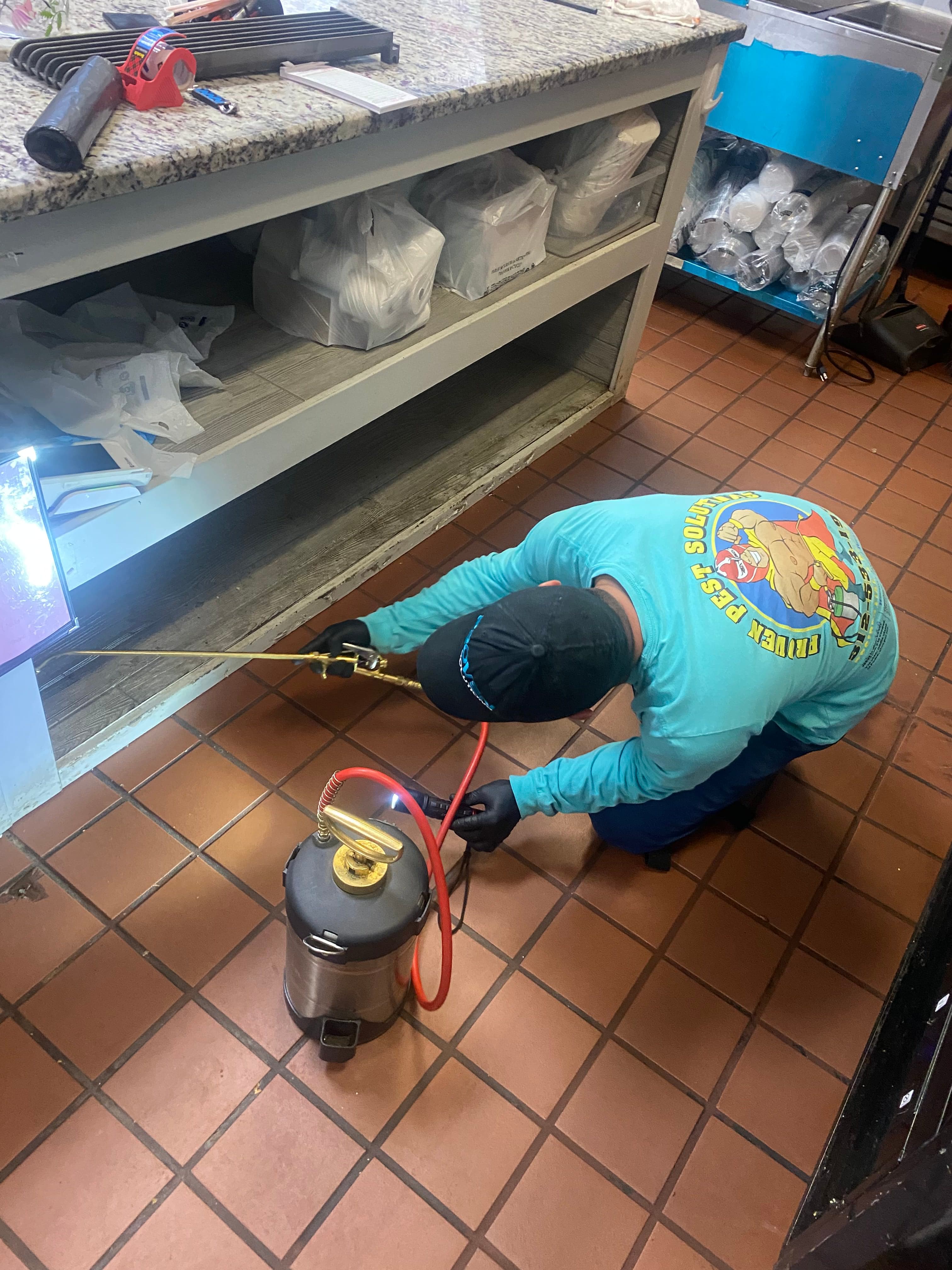 A pest technician inspecting beneath commercial kitchen shelving