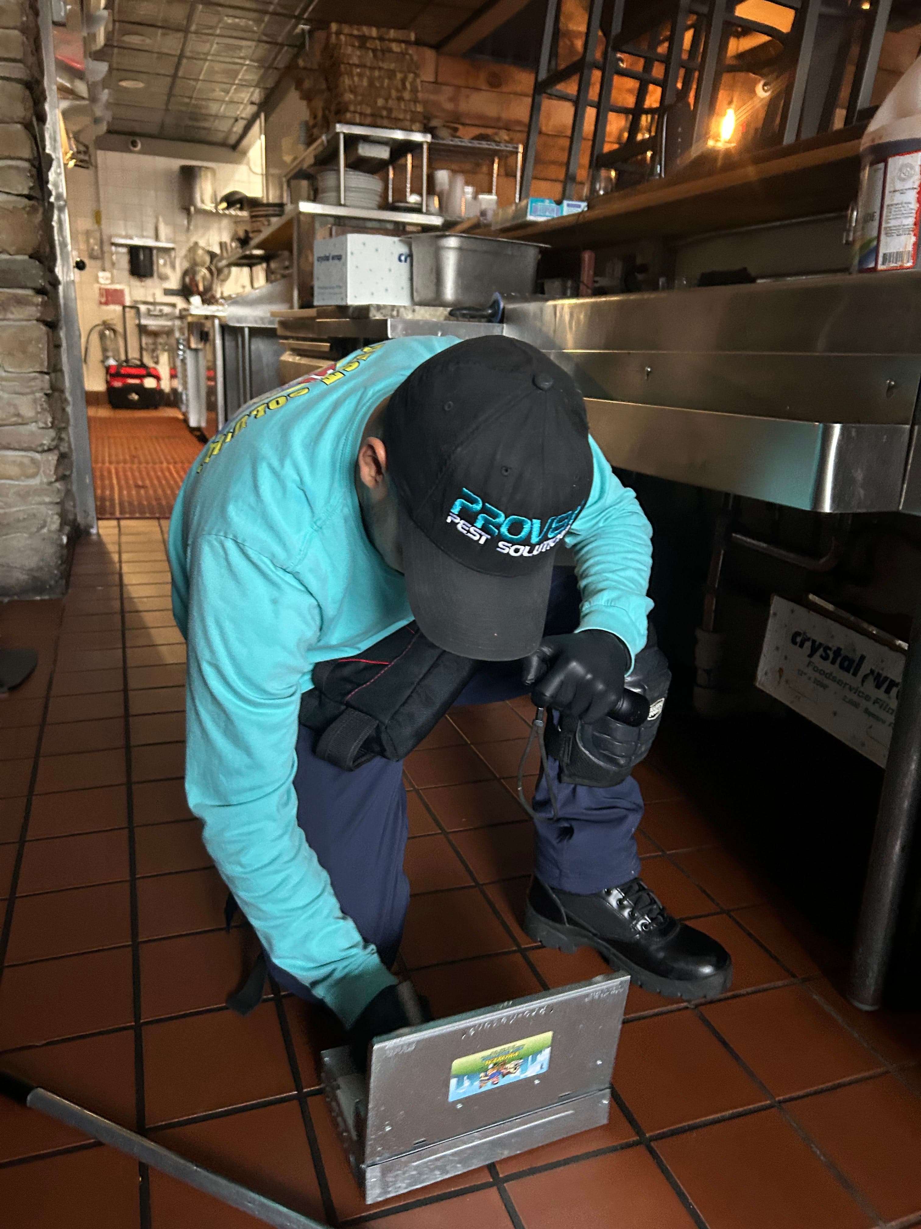 A pest technician inspecting beneath commercial kitchen equipment